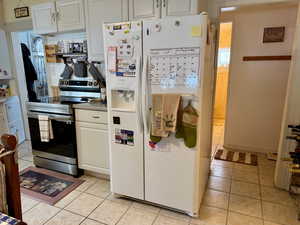 Kitchen with electric stove, white fridge with ice dispenser, white cabinetry, and light tile patterned floors