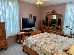 Bedroom with light colored carpet, ceiling fan, and a textured ceiling
