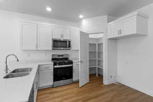 Kitchen featuring stainless steel appliances, light wood-style flooring, light stone countertops, and white cabinetry