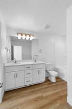 Bathroom with double vanity, light wood-style floors, and a textured ceiling