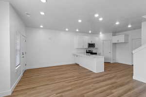 Kitchen with white cabinets, a peninsula, light countertops, light wood-type flooring, and recessed lighting