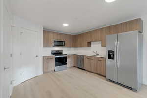 Kitchen featuring stainless steel appliances, light countertops, light wood-type flooring, modern cabinets, and recessed lighting