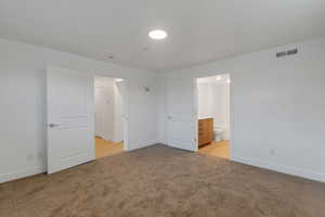 Unfurnished bedroom featuring light colored carpet and connected bathroom