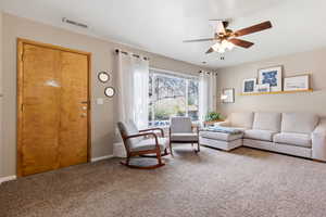 Carpeted living area featuring a ceiling fan and baseboards
