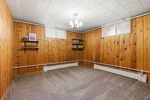 Carpeted empty room with a baseboard radiator, plenty of natural light, and wooden walls