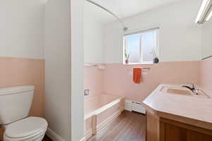 Full bathroom featuring wainscoting, tile walls, vanity, a baseboard heating unit, and dark wood-style floors