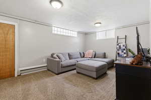 Carpeted living room featuring a baseboard heating unit, a textured ceiling, and plenty of natural light