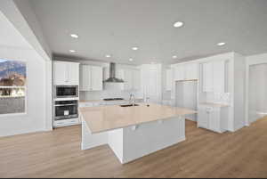 Kitchen featuring white cabinets, stainless steel appliances, a kitchen island with sink, light wood finished floors, and recessed lighting