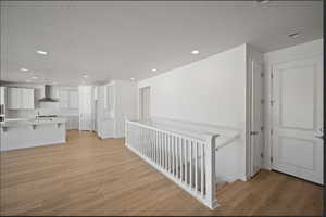 Corridor with light wood-style flooring, recessed lighting, a textured ceiling, and an upstairs landing