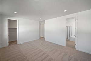 Unfurnished bedroom with a spacious closet, recessed lighting, light carpet, and a textured ceiling