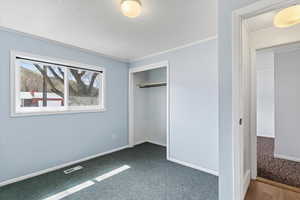Unfurnished bedroom with dark colored carpet, crown molding, a closet, and a textured ceiling