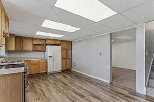 Kitchen featuring double oven range, a paneled ceiling, white refrigerator with ice dispenser, light countertops, and light wood-style floors