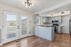 Kitchen with gray cabinets, light countertops, stainless steel appliances, a peninsula, and a tray ceiling