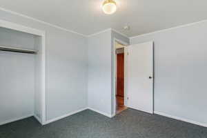 Unfurnished bedroom featuring dark carpet, a textured ceiling, ornamental molding, and a closet