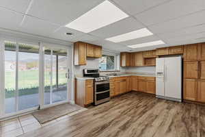 Kitchen featuring double oven range, white fridge with ice dispenser, a drop ceiling, light countertops, and light wood-type flooring