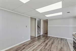 Finished below grade area featuring a drop ceiling, light wood-type flooring, and wooden walls