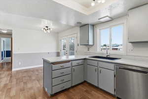 Kitchen with a textured ceiling, stainless steel dishwasher, gray cabinetry, dark wood-type flooring, and light countertops