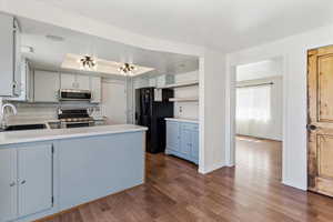 Kitchen with light countertops, stainless steel appliances, a raised ceiling, dark wood-style flooring, and a peninsula