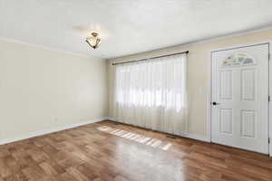 Entryway with a textured ceiling, wood finished floors, and crown molding