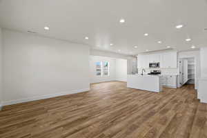 Kitchen featuring open floor plan, white cabinetry, light wood finished floors, a center island with sink, and recessed lighting