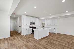 Kitchen featuring stainless steel appliances, white cabinetry, a center island with sink, light wood-type flooring, and recessed lighting