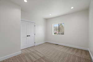 Unfurnished bedroom featuring light carpet, recessed lighting, and a closet