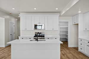 Kitchen featuring white cabinetry, stainless steel appliances, recessed lighting, light stone counters, and light wood-type flooring