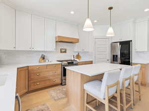 Dual tone kitchen featuring decorative backsplash, stainless steel appliances, two tone cabinets, light wood finished floors, and a breakfast bar area