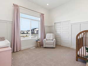 Bedroom with a decorative wall, a wainscoted wall, light carpet, and a crib