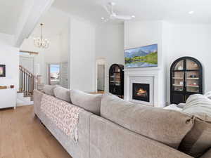 Living room with wood finished floors, a ceiling fan, vaulted ceiling, a glass covered fireplace, and a chandelier
