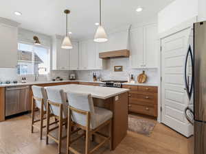 Kitchen featuring stainless steel appliances, a kitchen island, a kitchen bar, hanging light fixtures, and two tone cabinets