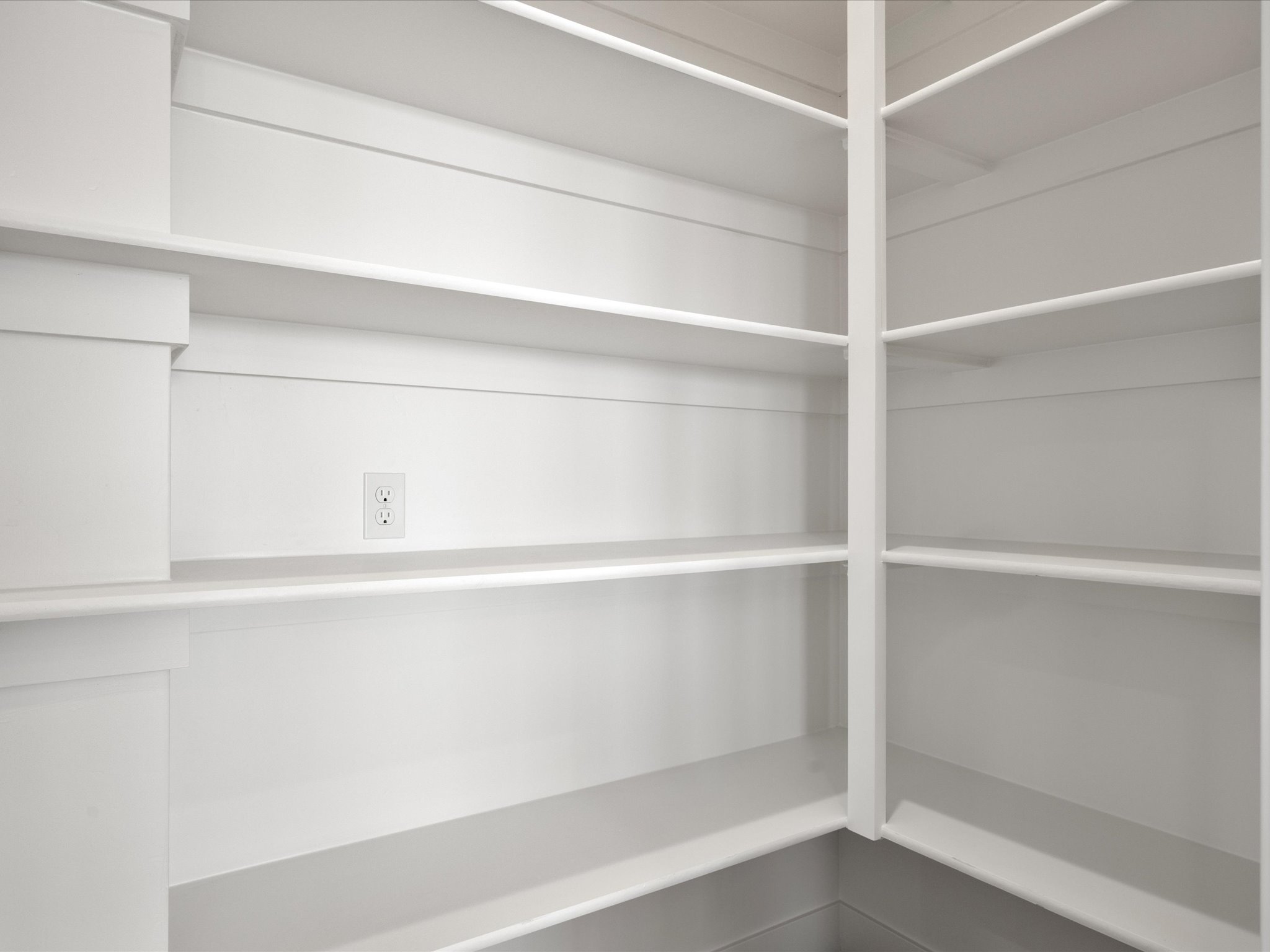 Pantry featuring extensive built-in shelving, white painted finish, and integrated electrical outlet