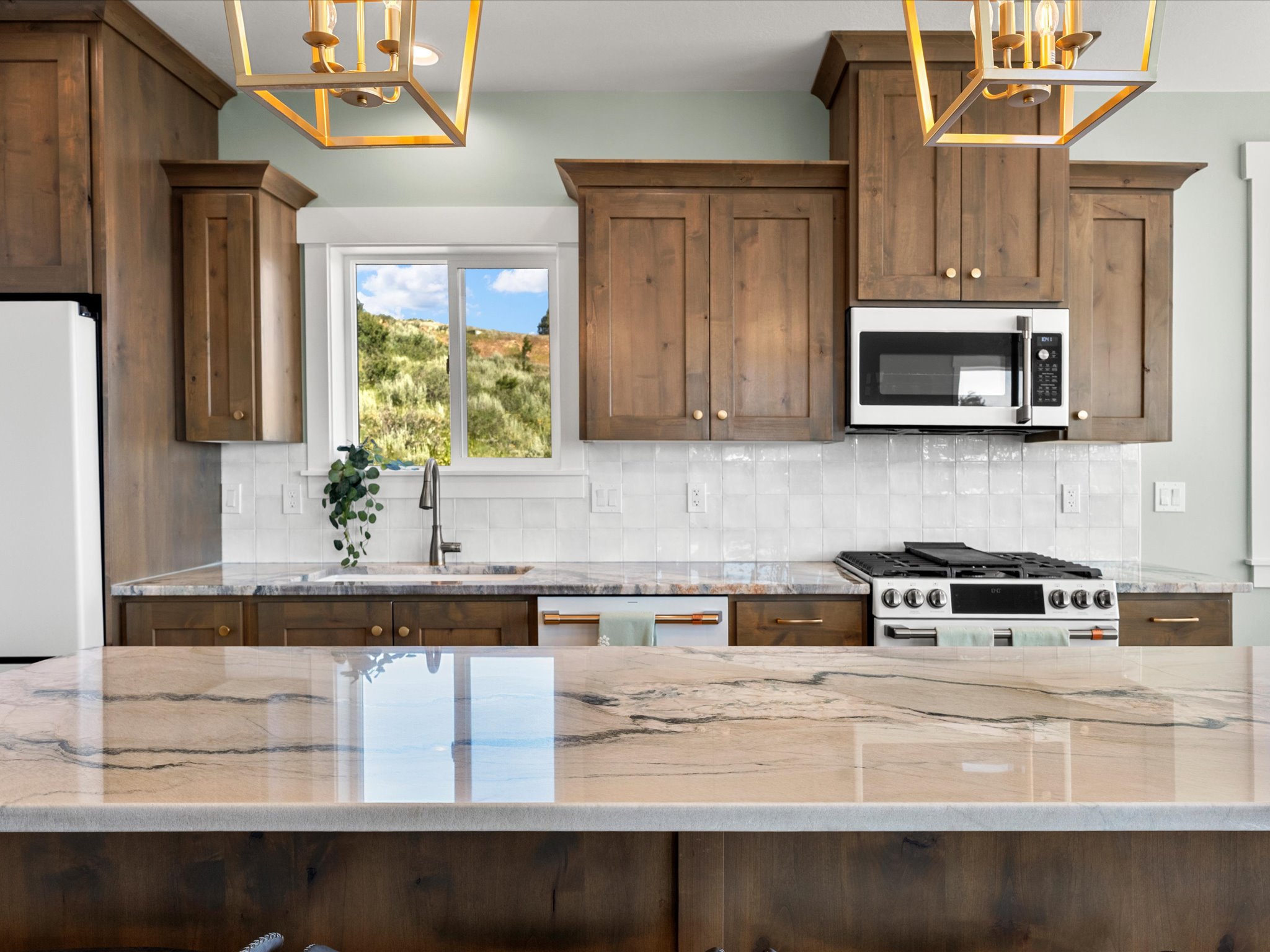 Kitchen featuring a large central island with a polished countertop, wood cabinetry, a tile backsplash, and stainless steel appliances including a range and built-in microwave