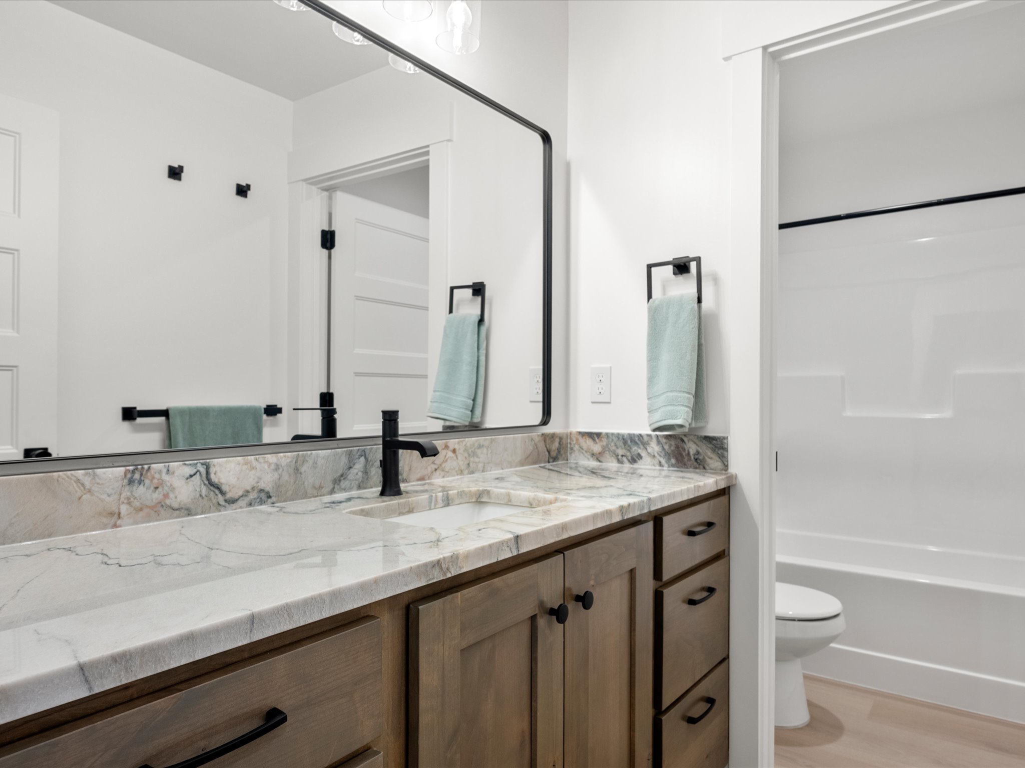 Bathroom vanity featuring a single sink with a matte black faucet, stone countertop with natural veining, and wood-finish cabinetry