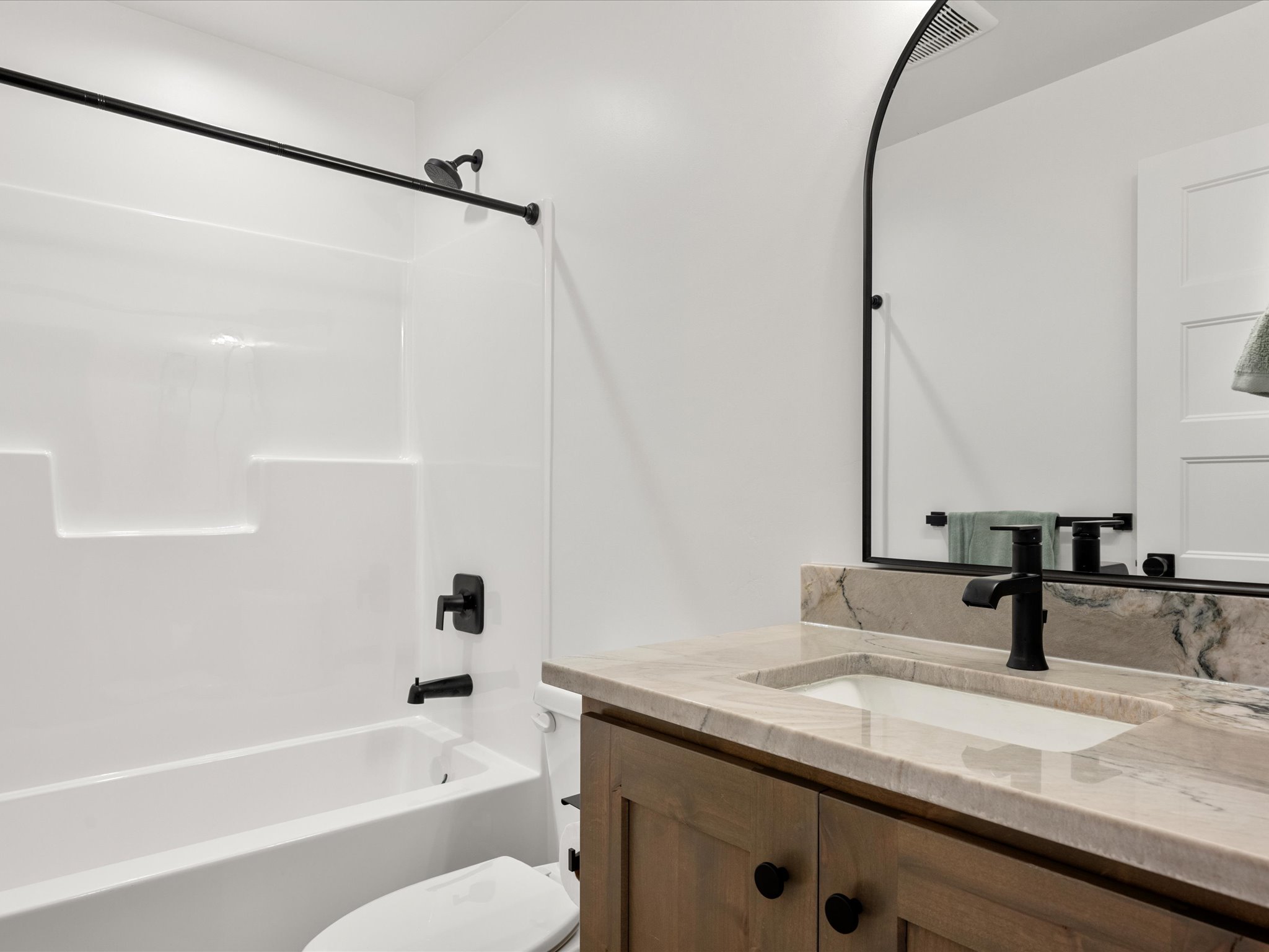 Bathroom featuring a wood-finish vanity with an undermount sink, stone countertop, and matte black fixtures