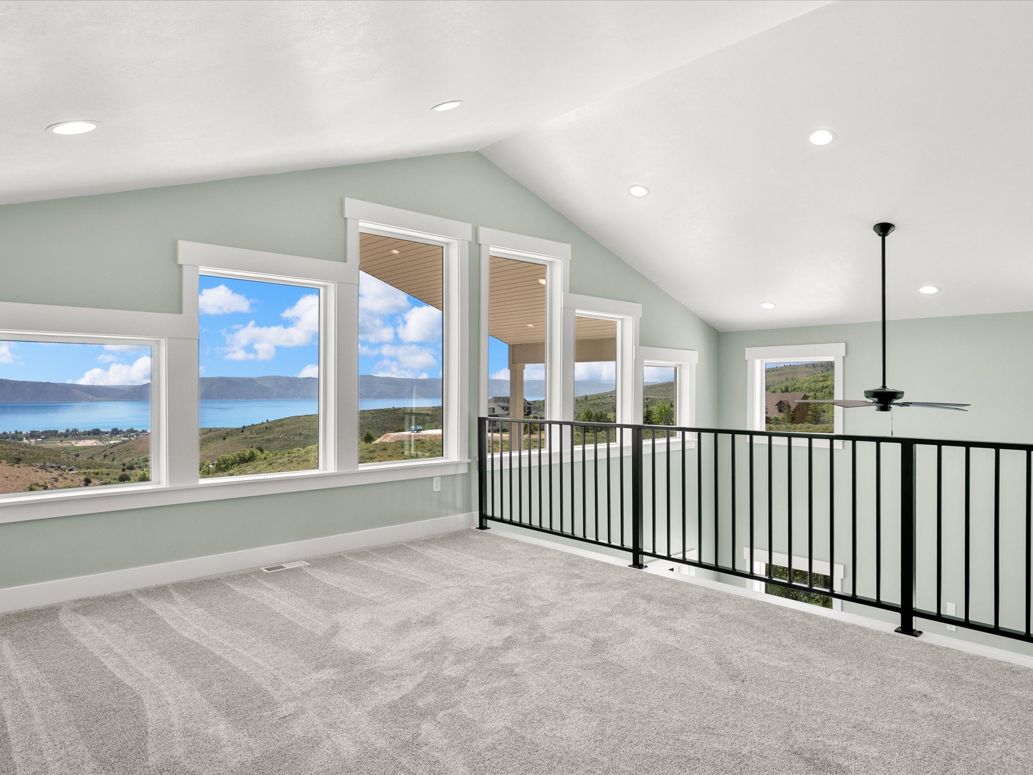 Spacious upper-level room featuring expansive windows, vaulted ceilings, recessed lighting, and soft grey carpeting