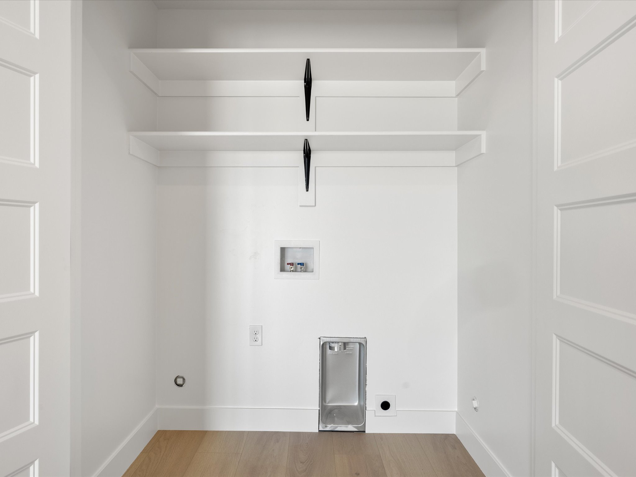 Dedicated laundry space featuring two built-in shelves, wood-finish flooring, and crisp white trim