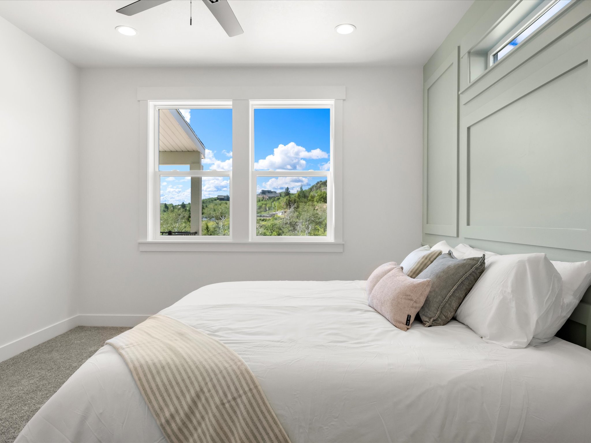 Bedroom featuring light-toned carpeting, a window wall with white trim, and a contemporary ceiling fan