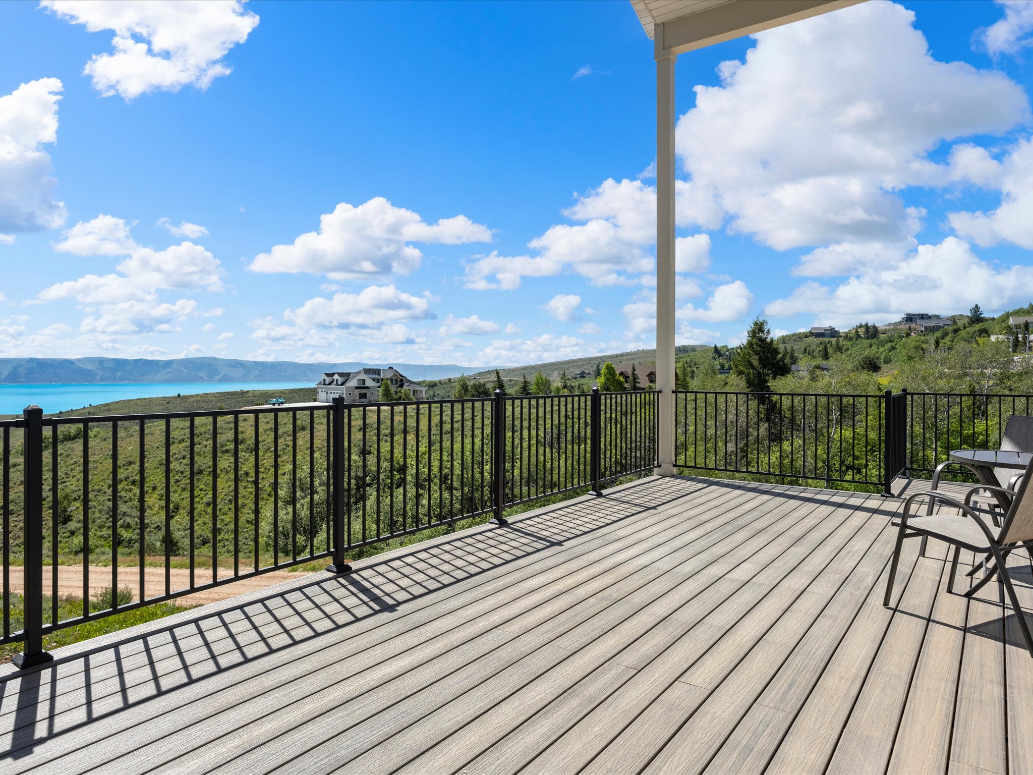 Spacious outdoor deck featuring composite decking, black metal railings, a partial overhead patio cover, and expansive water scenery with distant mountains