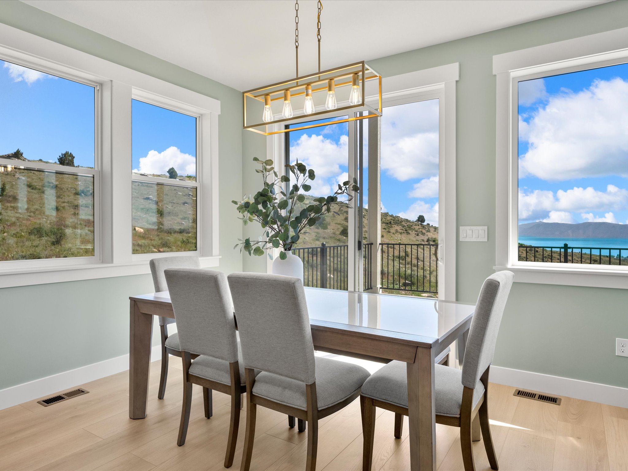 Dining area featuring light wood-finish flooring, a contemporary linear chandelier, and a sliding glass door leading to a balcony with a black metal railing