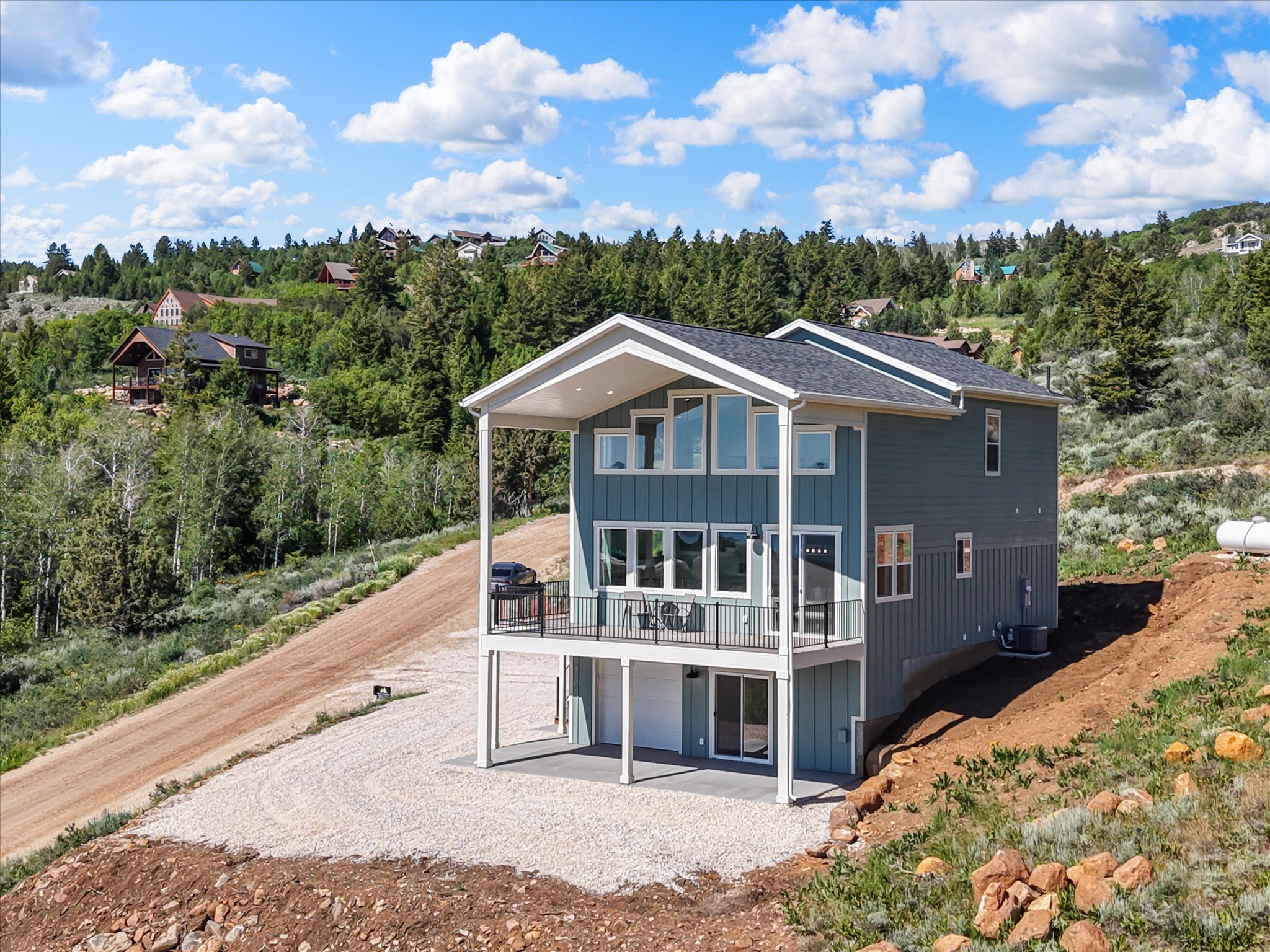 Modern two-story residence featuring a covered balcony, an abundance of windows, a lower-level patio, and a gravel driveway