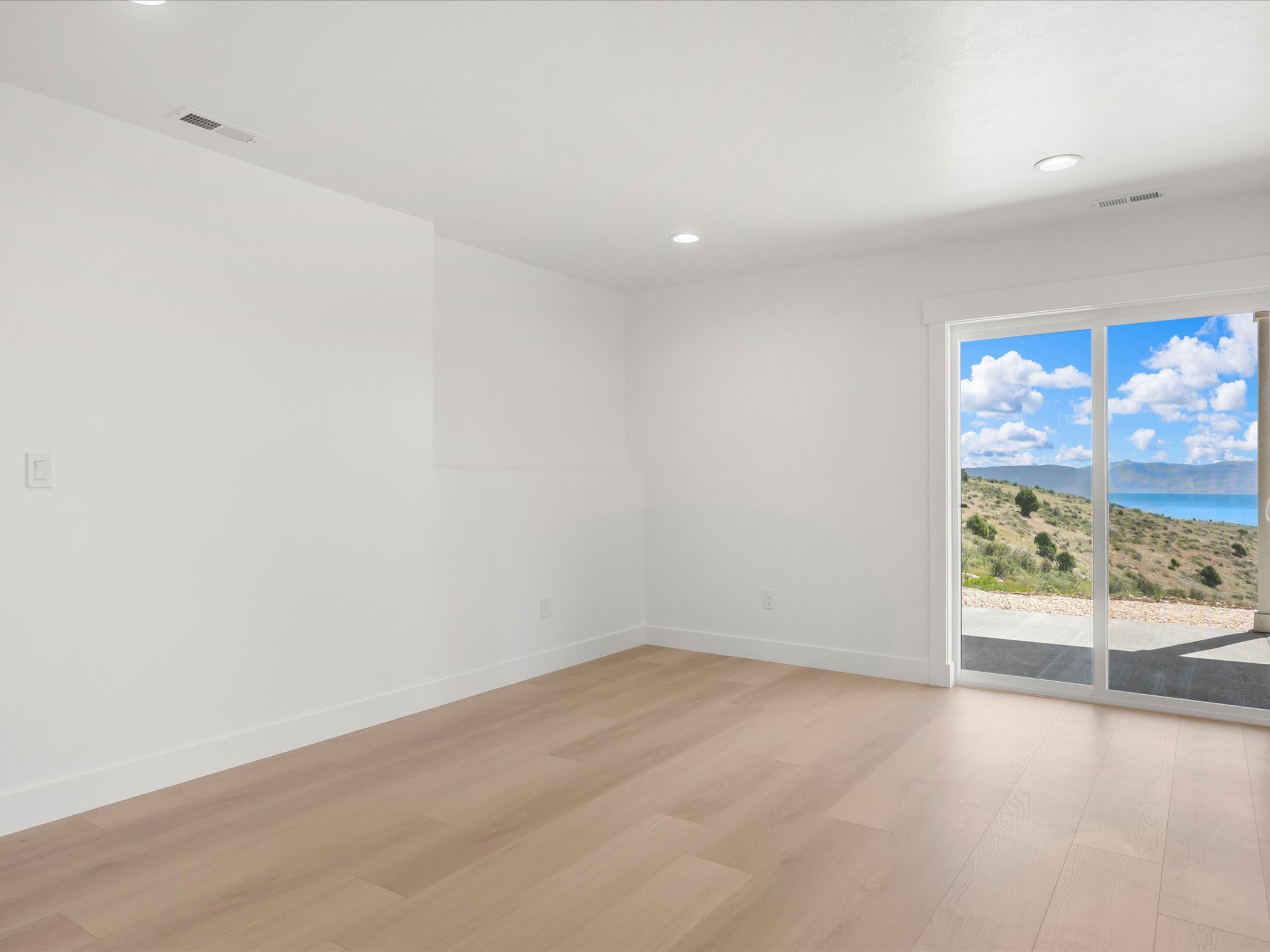 Bright interior space featuring a glass sliding door, light wood-finish flooring, recessed lighting, and white baseboards