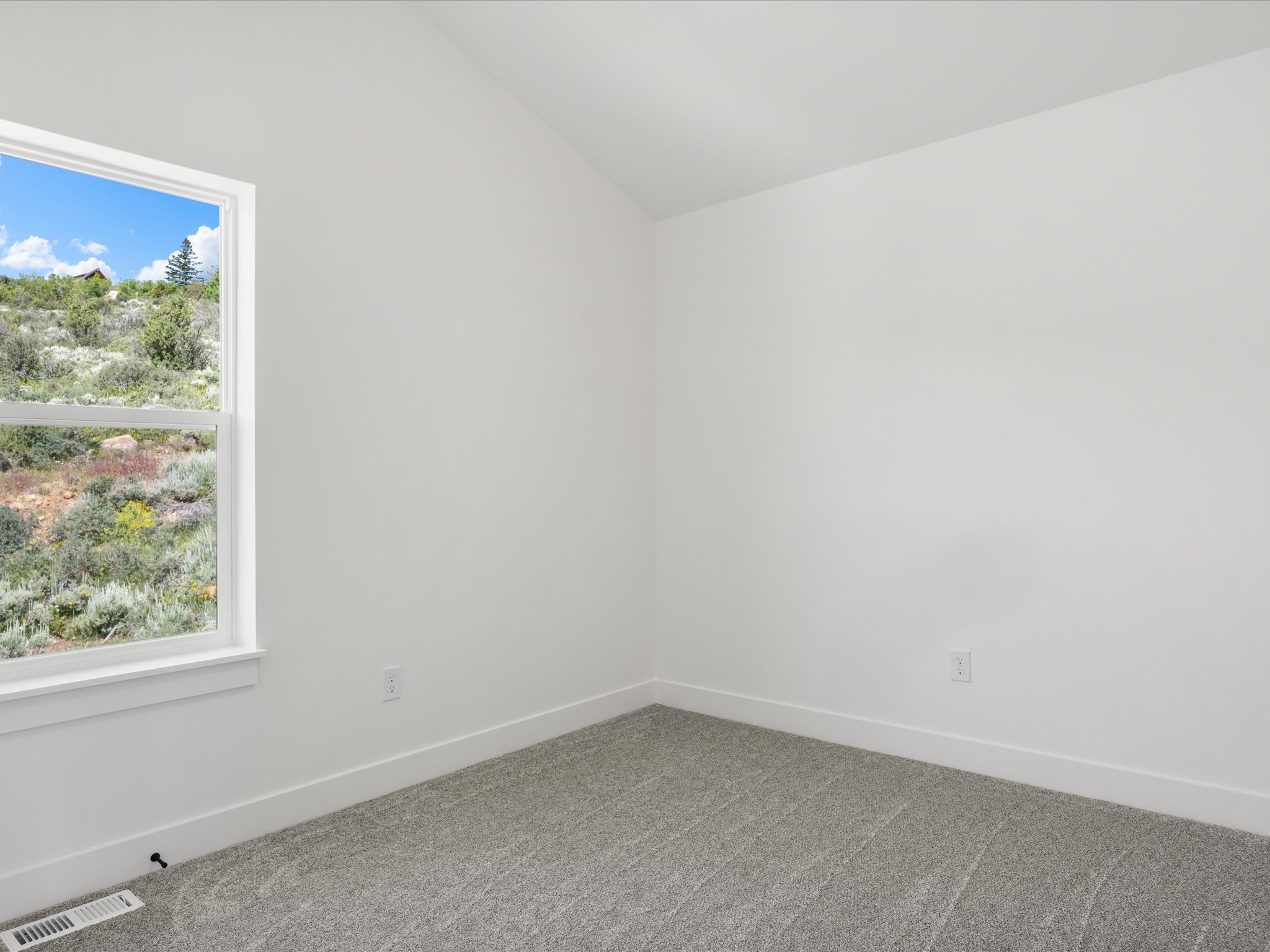 Room featuring a single double-hung window, sloped ceiling, light gray carpeting, crisp white walls, and white baseboards