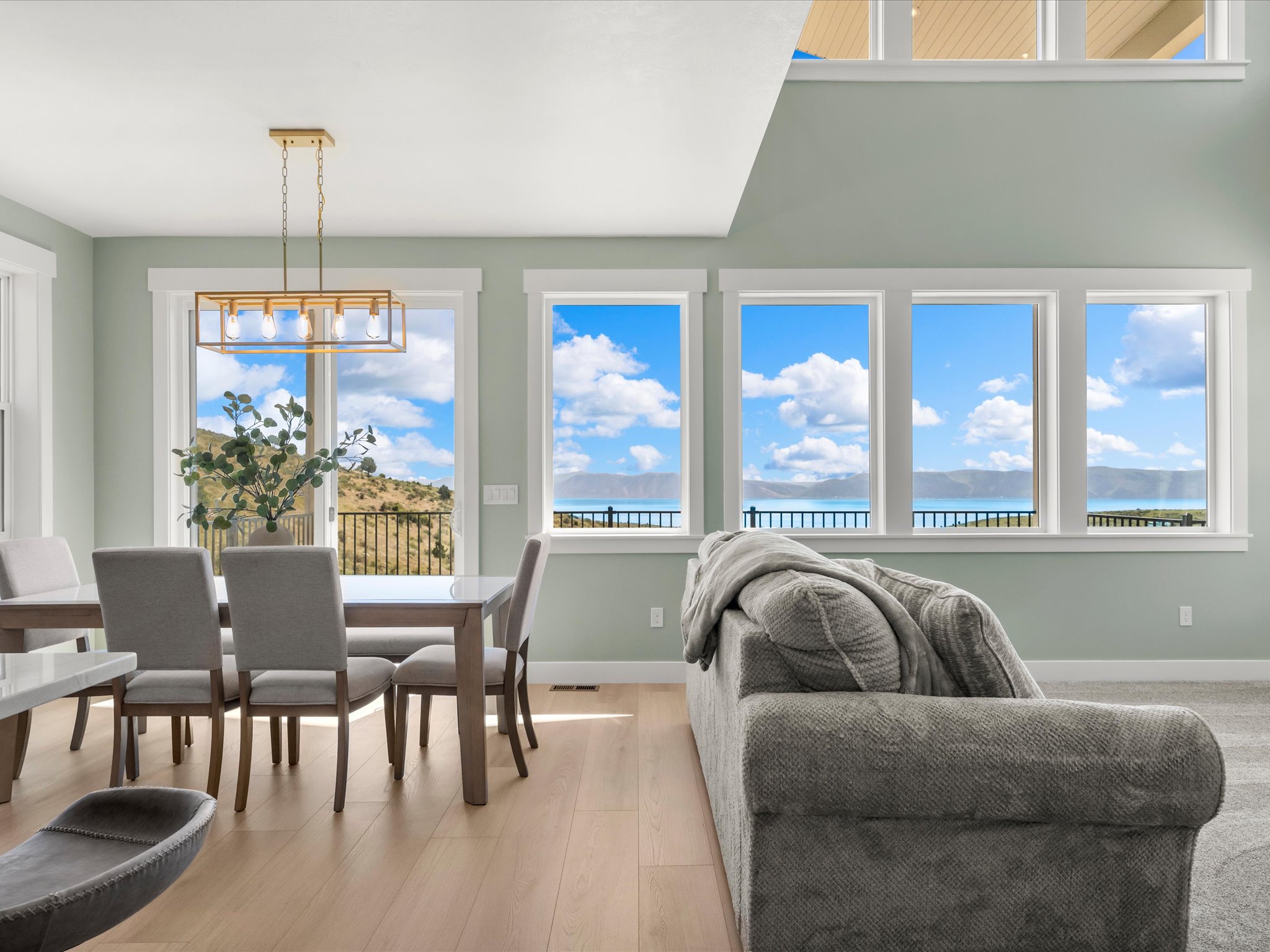 Open-concept living space with expansive wall of windows, high ceilings, wood-finish flooring, and a modern rectangular chandelier