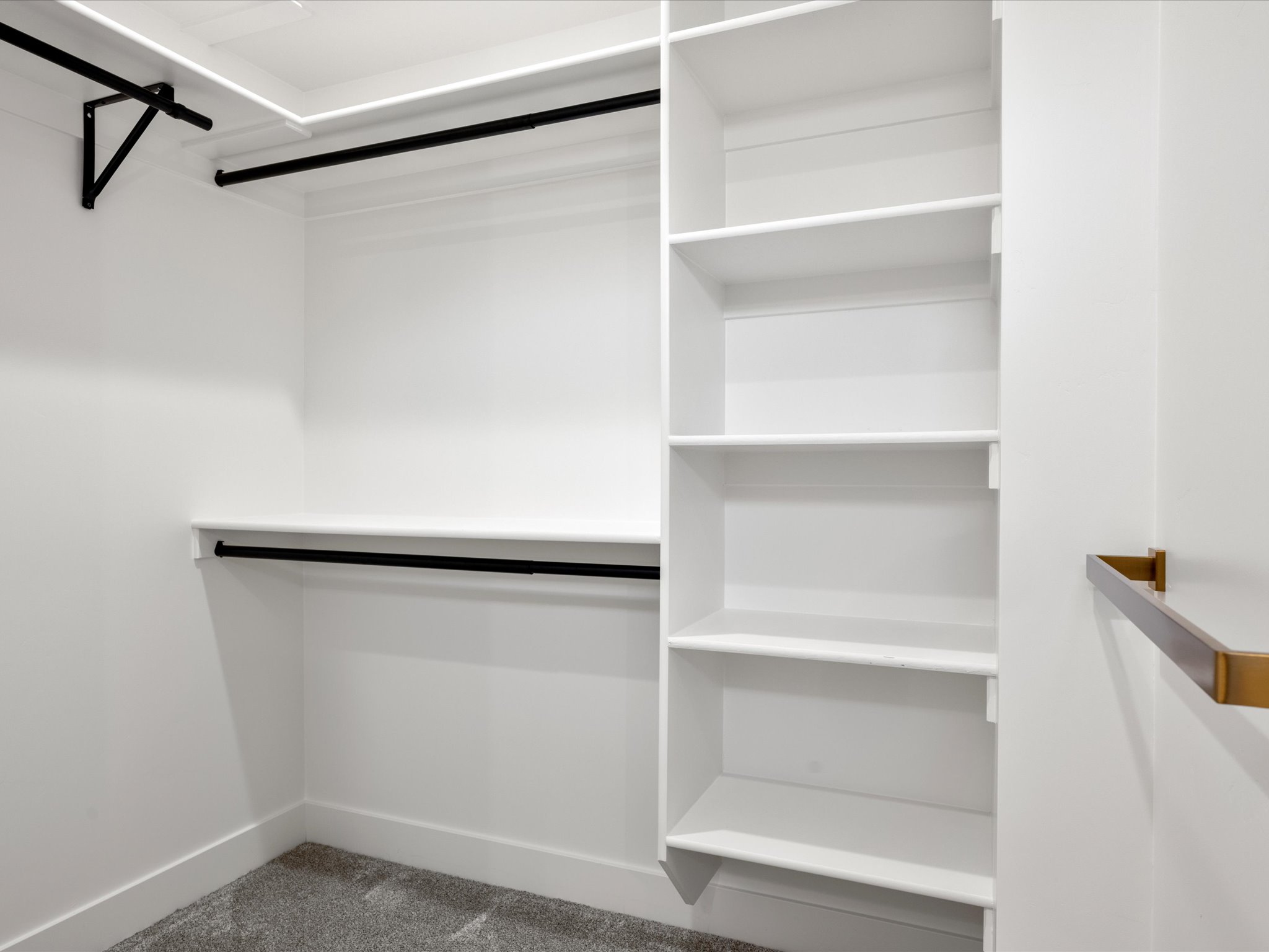 Custom closet organization system featuring white shelving, black hanging rods, and a built-in shelving unit
