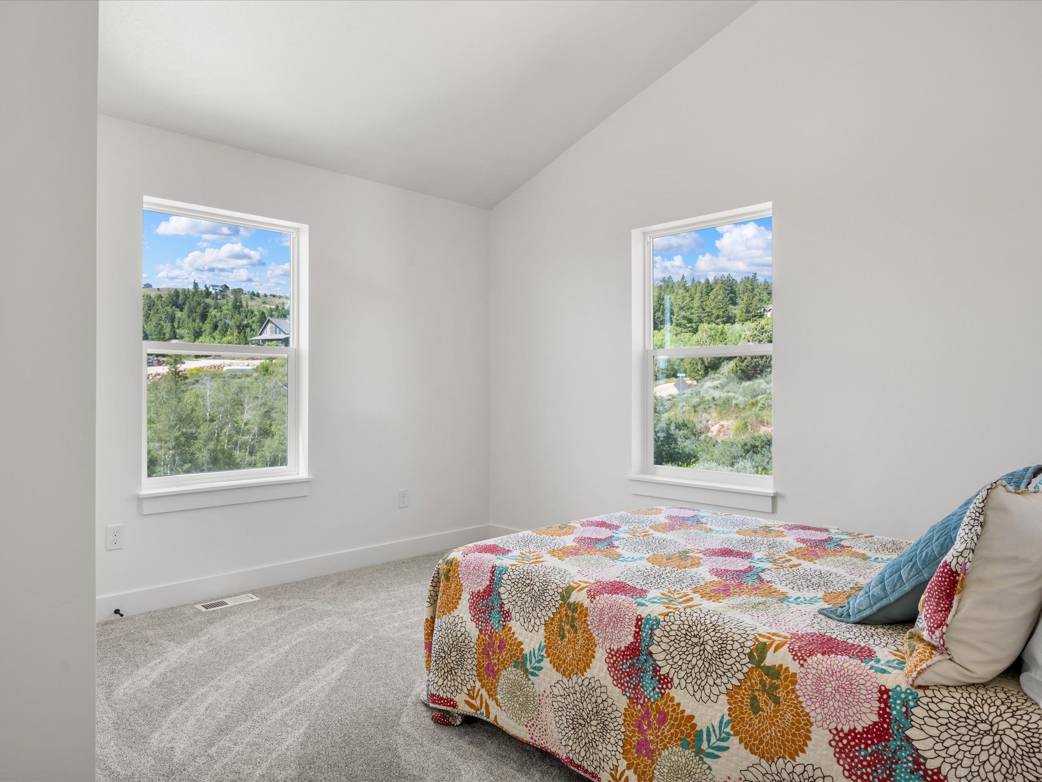 Bright interior space featuring two large windows, a vaulted ceiling, light gray carpeting, and white baseboards