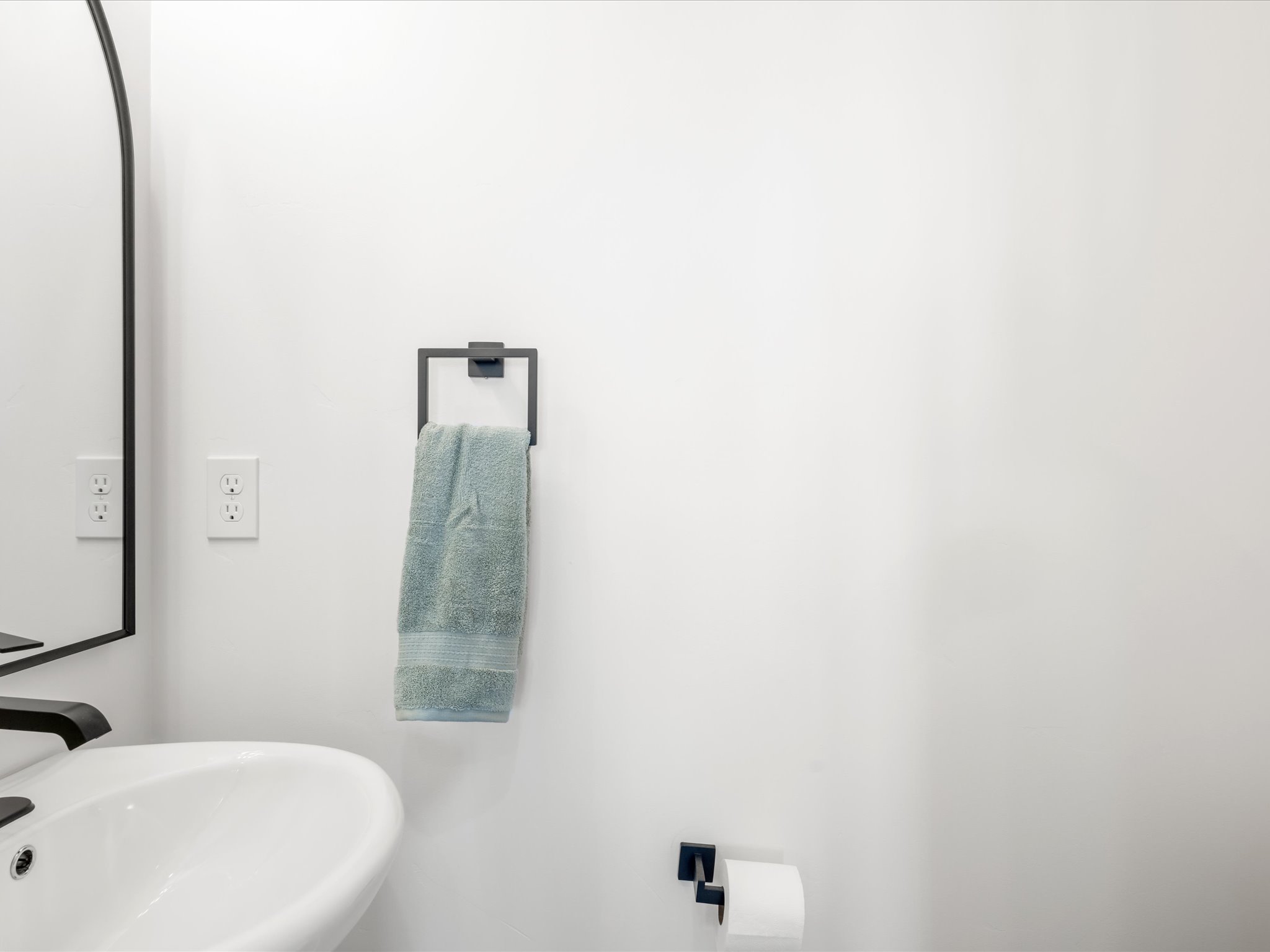 Pedestal sink with a matte black faucet, complemented by a contemporary wall-mounted mirror