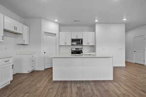 Kitchen with white cabinetry, stainless steel appliances, dark wood-style floors, recessed lighting, and a center island with sink