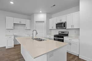 Kitchen featuring a center island with sink, stainless steel appliances, white cabinets, dark wood finished floors, and recessed lighting