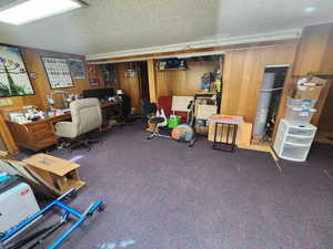 Office space with a textured ceiling, water heater, wood walls, and dark carpet